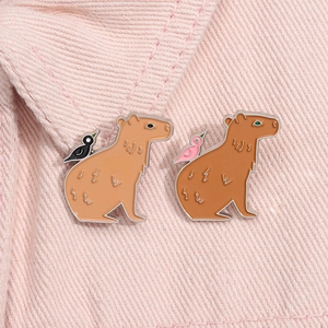 Gros plan de pin's capybara en émail avec oiseaux sur un tissu en denim rose pastel