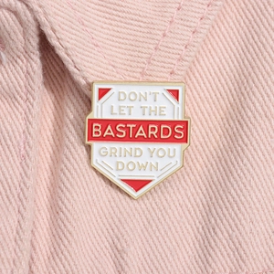 Macro view of shield-shaped enamel pin with quote on pink denim fabric background