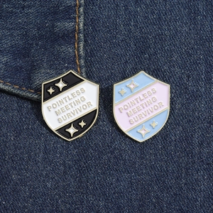 Detail of shield-shaped enamel pins with Pointless Meeting Survivor text on denim