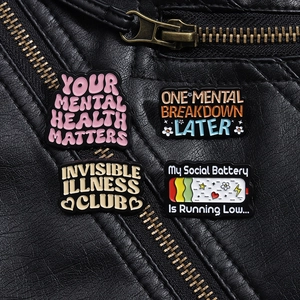 Emaille-Pins mit Sprüchen zur psychischen Gesundheit auf einer Lederjacke