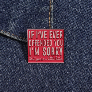 Detail of red enamel badge pinned on denim fabric showing a humorous English quote