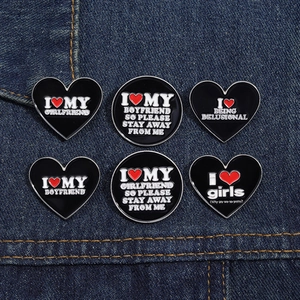 Close-up of black enamel heart brooches with white text on a blue denim background