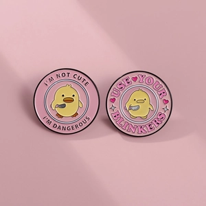 Close-up of yellow duck enamel pins with I'm Not Cute and Use Your Blinkers text