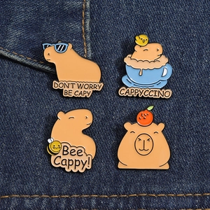 Detailed set of four cute enamel capybara badges pinned on blue denim fabric background