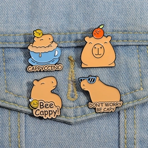 Close-up of four cute cartoon capybara enamel pins on a blue denim background