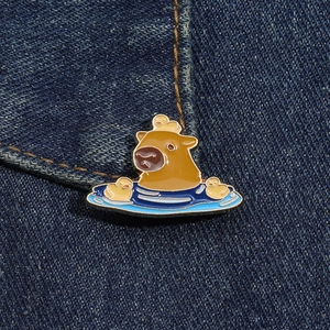 Close-up of enamel capybara and ducks pin displayed on blue denim jacket texture