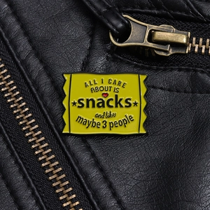 Close-up of a bright yellow enamel snack bag brooch with black text on a black leather jacket