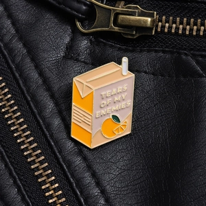 Close-up of orange juice enamel pin with Tears of My Enemies text on a black leather jacket