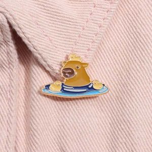 Close-up of cute enamel capybara brooch with yellow ducks on pink fabric texture