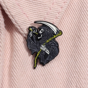 Macro view of a black Grim Reaper enamel pin with a silver scythe on pink corduroy