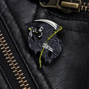 Close-up of a Grim Reaper enamel pin with scythe on a black leather jacket texture