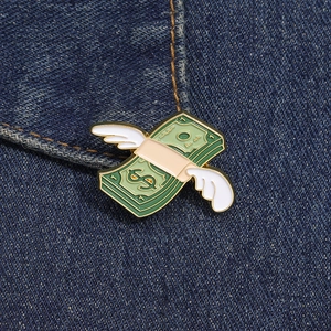 Dettaglio della spilla smaltata con banconota volante su sfondo di denim blu