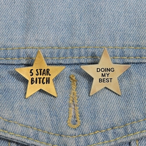 Detail of star-shaped metal enamel pins with slogans pinned on blue denim fabric