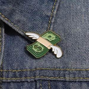 Dettaglio della spilla smaltata con banconota volante su tessuto in denim blu scuro