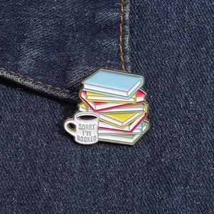 Dettaglio della spilla smaltata con libri colorati e tazza di caffè su tessuto denim