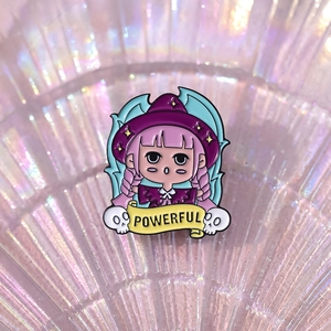 Detail of pink-haired wizard girl enamel pin with a yellow scroll reading POWERFUL
