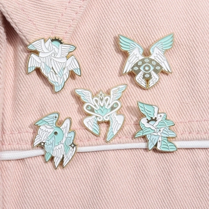 Close-up of five white enamel feather wing and eye pins on pink denim fabric surface