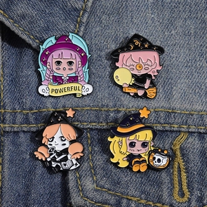 Close-up of four cute anime girl enamel pins displayed on blue denim fabric background