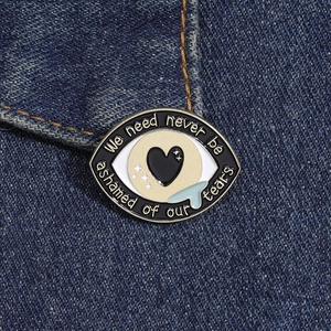 Macro d'un pin's oeil en émail avec cœur et larmes sur tissu denim bleu foncé