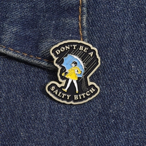 Detail of metal enamel pin featuring a girl in yellow raincoat with blue umbrella