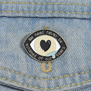 Détail de la broche œil en émail sur denim avec texte 'We need never be ashamed of our tears'