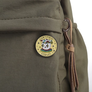 Close-up of a colorful Certified Clown enamel pin on a green canvas bag background