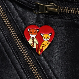 Detail of heart enamel pin with fox characters on black leather jacket texture