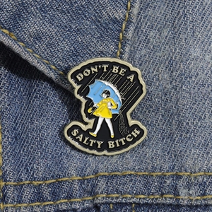 Macro shot of an enamel pin featuring a girl in a yellow dress walking in the rain