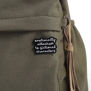Detail einer schwarzen Emaille-Anstecknadel mit weißem Text an einem grünen Rucksack