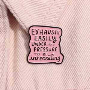 Makroaufnahme einer rosa Emaille-Anstecknadel mit kreativem Spruch auf Denim-Stoff