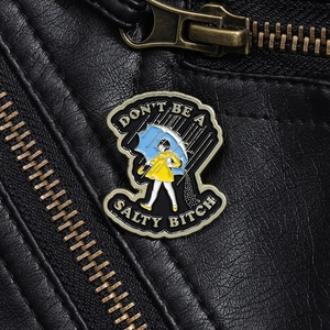 Detail of creative girl in yellow raincoat enamel pin on black leather jacket