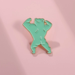 Close-up of muscular cartoon frog enamel pin with gold plating on pink background
