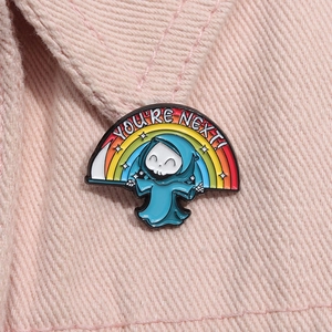 Dettaglio della spilla smaltata con piccolo mietitore, arcobaleno e testo You're Next su jeans