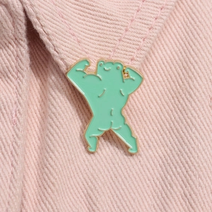 Detailed view of muscle frog enamel pin with gold edges on pink denim fabric