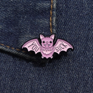 Detail of pink bat enamel pin with You Suck text on denim jacket for Halloween