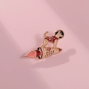 Detail shot of Soviet Laika space dog enamel pin with CCCP rocket on pink background