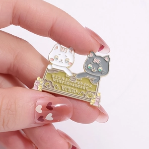 Vista dettagliata delle spille gatto in smalto con design tavola Ouija tra le dita