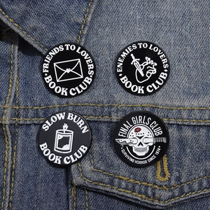 Detailed view of four black enamel pins with white text pinned to a blue denim jacket