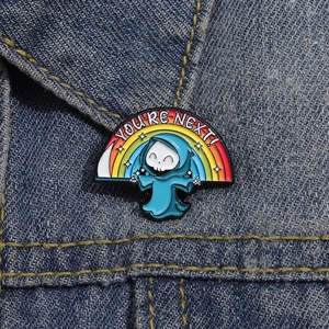 Detailed close-up of a rainbow reaper enamel pin on a blue denim jacket with You're Next text