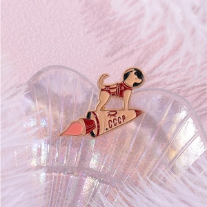 Macro shot of CCCP Soviet space dog enamel pin on a decorative shell and feather backdrop