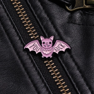 Detail of pink bat enamel pin with You Suck text pinned on a black leather jacket