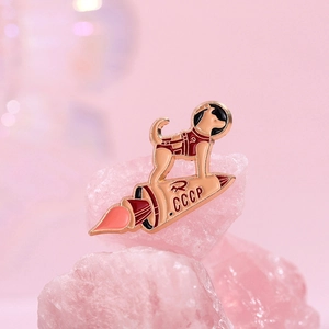 Space dog enamel pin on a retro rocket with CCCP lettering on pink quartz stone