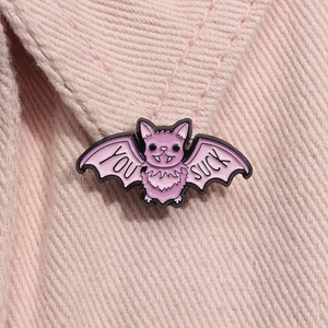 Close-up of pink bat enamel pin with YOU SUCK text on light pink denim fabric