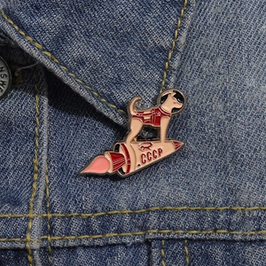 Close-up of a Soviet space dog enamel pin featuring a rocket and CCCP logo on denim