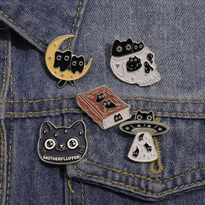 Detail of five Halloween black cat enamel pins on denim, showing cats, skulls, and a UFO