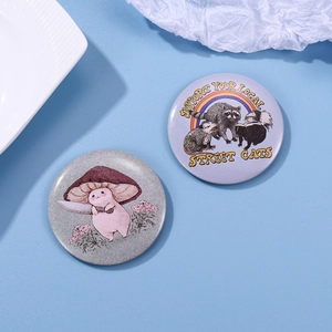 Detail of two tinplate badges featuring mushroom illustration and street cat text theme