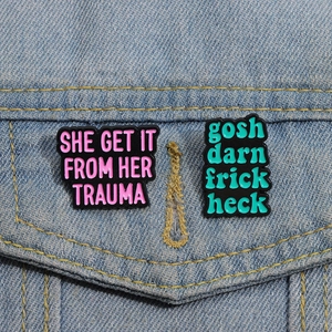 Detail view of two enamel pins with funny slogans on a blue denim jacket pocket