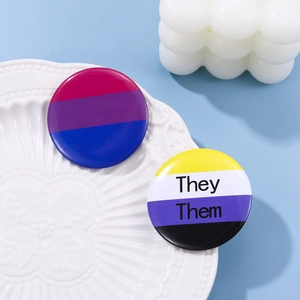 Close-up of bisexual and non-binary pride tinplate badges with They Them pronouns