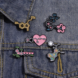 Detailed view of pink heart chemical formula enamel pins on dark blue denim fabric
