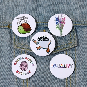 Close-up of five colorful round tinplate badges featuring diverse meme designs on denim